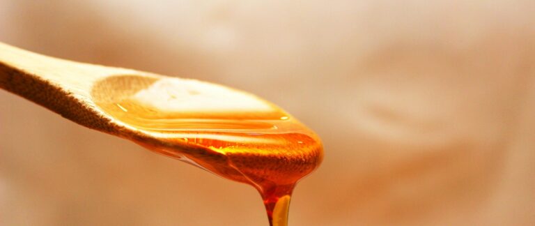 Macro shot of golden honey pouring from a wooden spoon, emphasizing its rich texture and color.